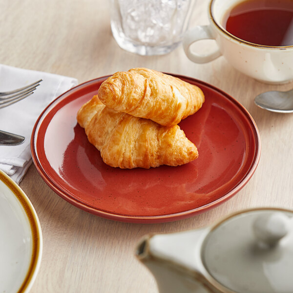 An Acopa Keystone Sedona Orange coupe plate with a croissant and a cup of tea on it.