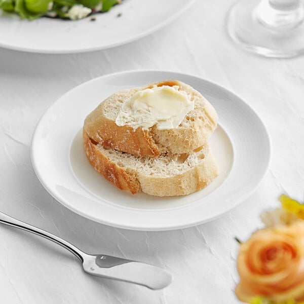 An Acopa Liana bright white porcelain plate with embossed lines, containing a piece of bread with butter on it.