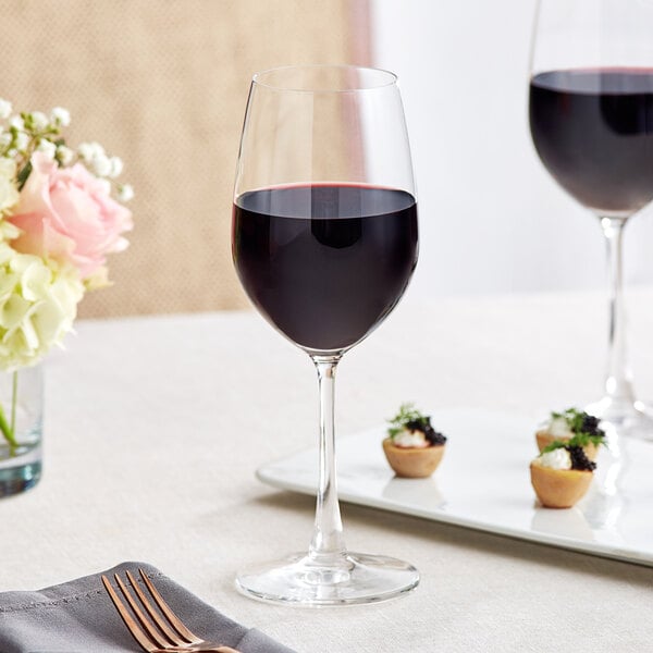 An Acopa Covella wine glass filled with red wine on a table with flowers.