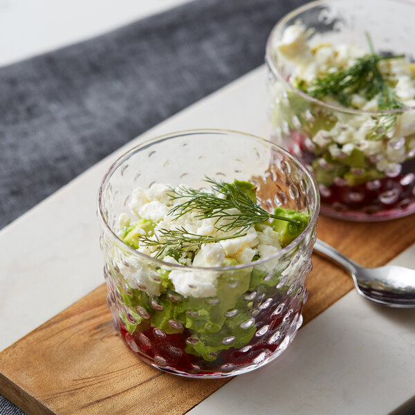 Two Acopa hobnail glass bowls filled with food on a white background.