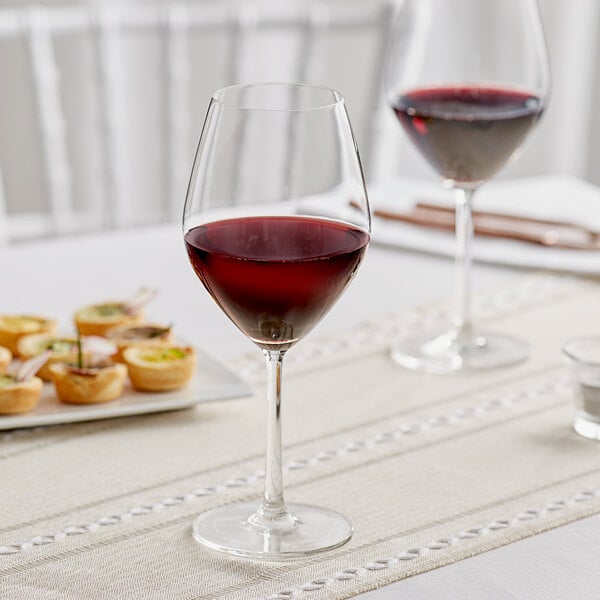 Two Acopa Bordeaux wine glasses of red wine on a table.