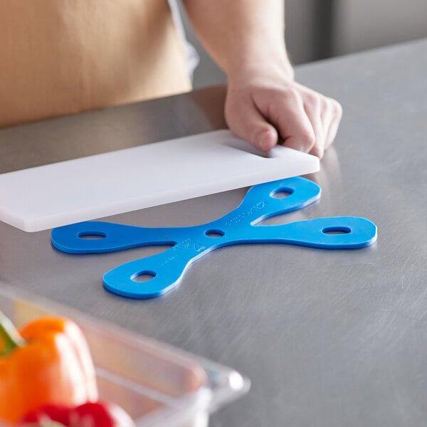 A person cutting vegetables with a blue Mercer Bar Buddyz cutting board on a white counter.