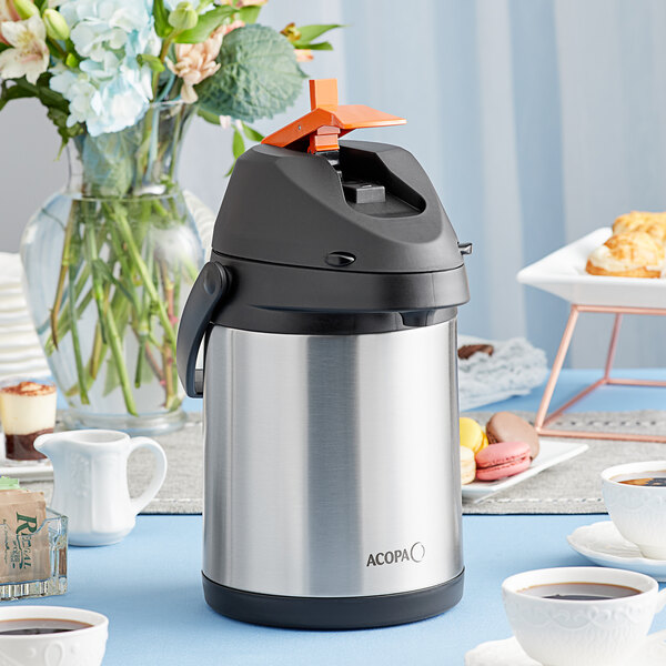 An Acopa stainless steel decaf airpot on a table with a cup of coffee.