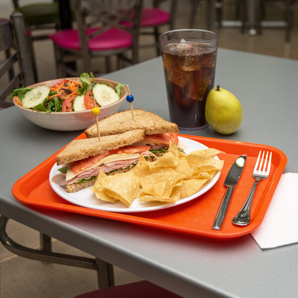 A Carlisle orange plastic fast food tray with a sandwich and chips on it.