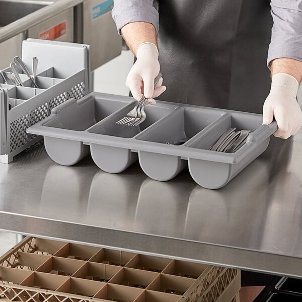 A person holding a tray of silverware using a grey Choice plastic flatware bin.