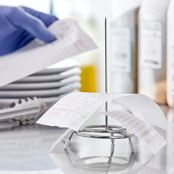 A person using a Choice chrome check spindle to hold a receipt on a counter.