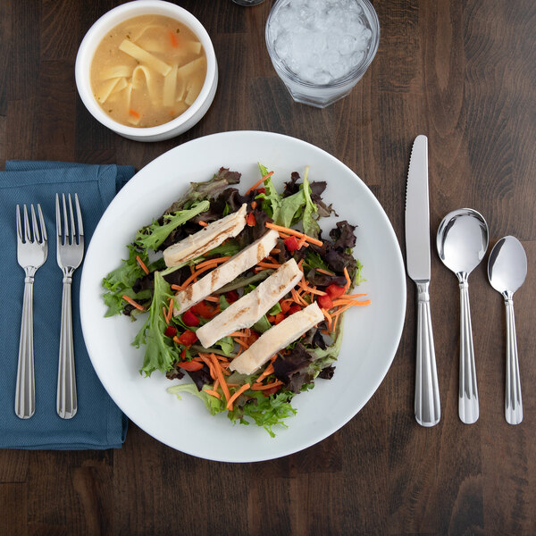 A plate of salad with chicken and vegetables on Acopa Harmony flatware.