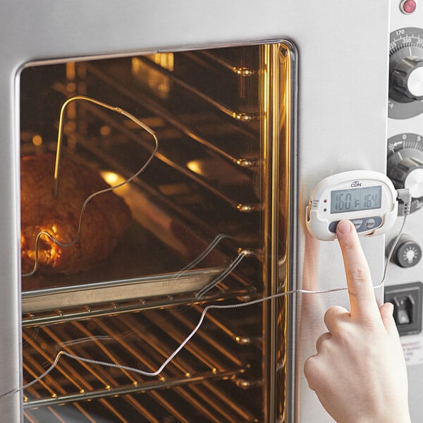 A hand holding a CDN digital probe thermometer to food in an oven.