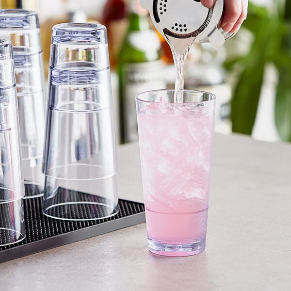 A person pouring pink liquid from a strainer into a Choice clear plastic glass.