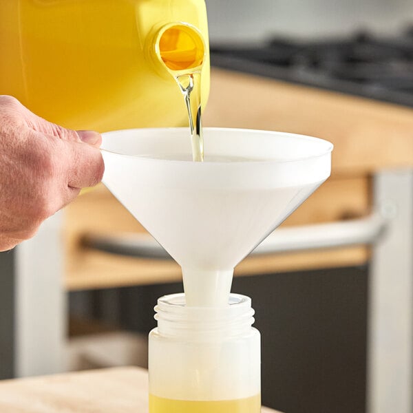 A white plastic funnel being used to pour liquid from a yellow container into a bottle.