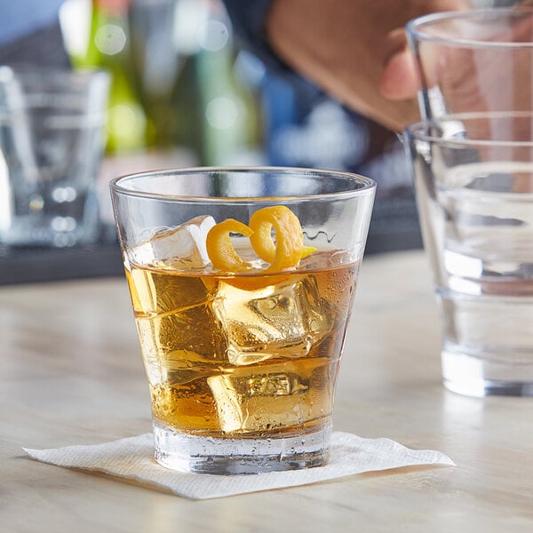 A person holding an Acopa Select Flared Rocks glass with whiskey, ice, and an orange peel.