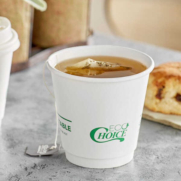 A hand holding a cup of tea with a white EcoChoice paper cup and a tea bag in it.