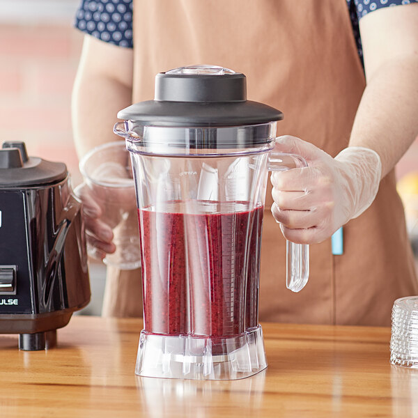 A person holding a Waring blender with a red smoothie inside.
