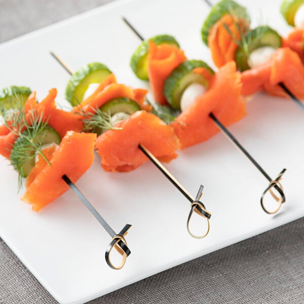 A close-up of a skewer with salmon and cucumber on a white plate.