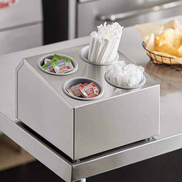 A stainless steel flatware organizer with gray plastic cylinders holding utensils on a counter.