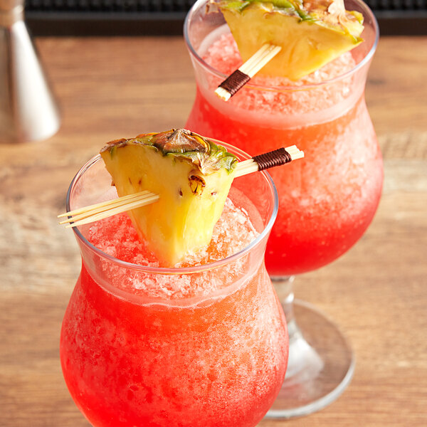 Two glasses with a drink and pineapple slices on bamboo skewers.