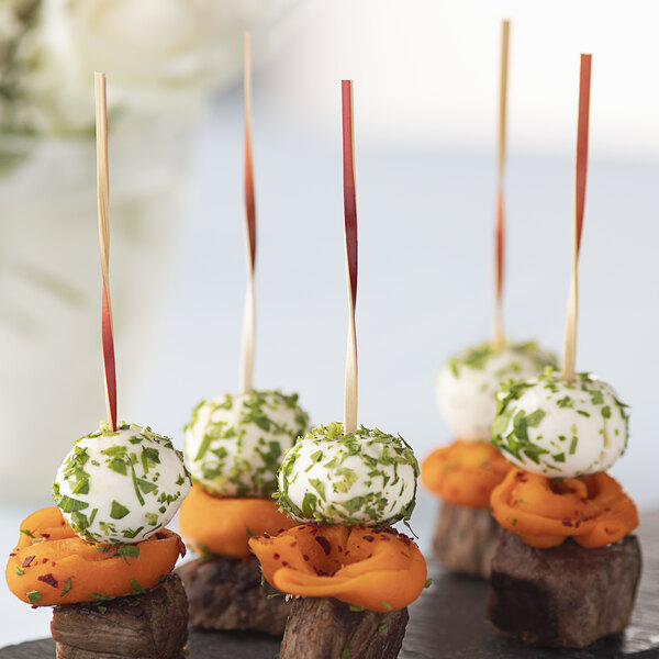 A plate of meat appetizers with red bamboo skewers on a table.