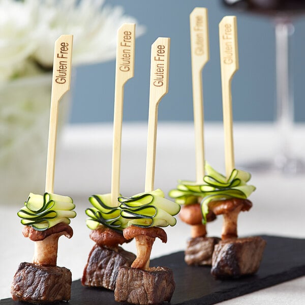 Bamboo food picks with steak and cucumber slices on a black plate.