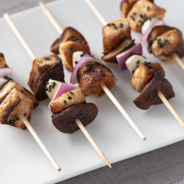 A wooden skewer with chicken and mushrooms on it served on a plate.