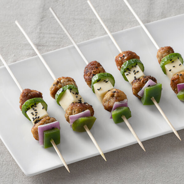 A plate with skewers of meatballs and vegetables on sticks.