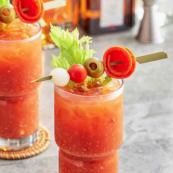 A bloody mary garnished with a green olive and a tomato on a bamboo skewer.