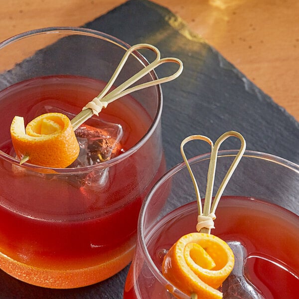 Two glasses of liquid with Bamboo Heart Skewers and orange spirals on a table in a cocktail bar.