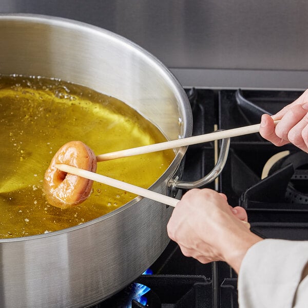 Donuts being fried in a large stock pot of canola oil