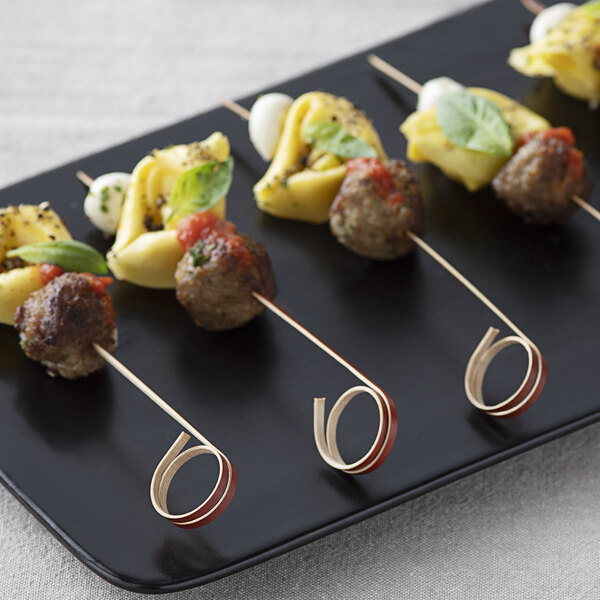 A black tray with red bamboo skewers of meat and vegetables on a table.