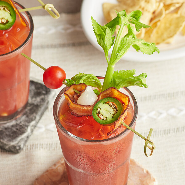 Two drinks with cherry tomatoes and jalapenos on bamboo skewers.