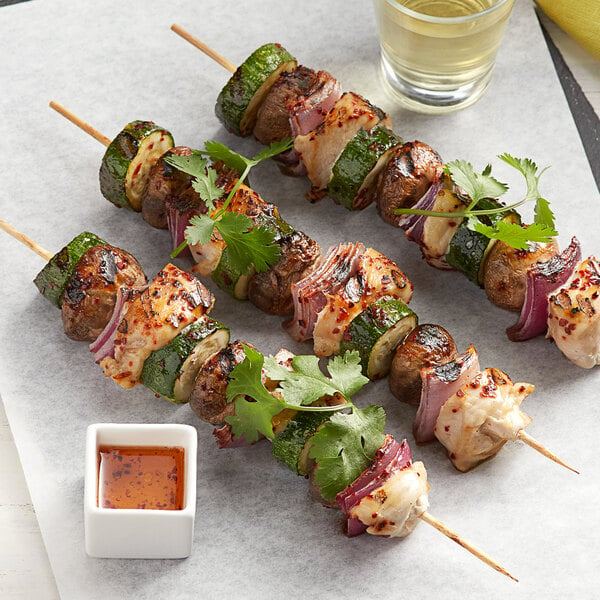 EcoChoice bamboo skewers with chicken and vegetables and a cup of sauce on a white surface.