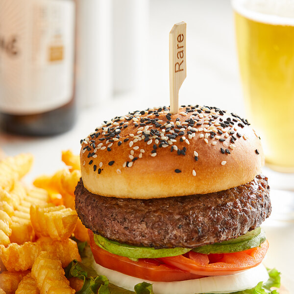 A burger with a Bamboo by EcoChoice "Rare" Meat Marker on top, served with fries on a plate.
