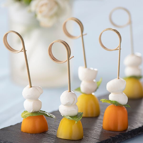 A black plate with a group of Bamboo Loop Food Picks holding fruit and cheese.