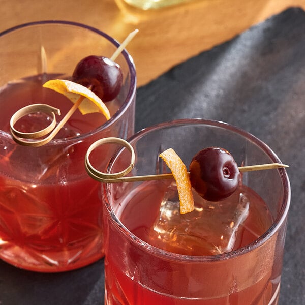 A red cocktail with a cherry and bamboo skewer on a table.