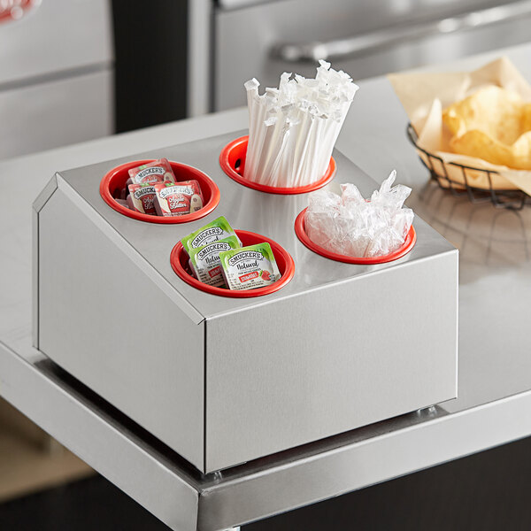 A stainless steel flatware organizer with red plastic cylinders holding utensils.