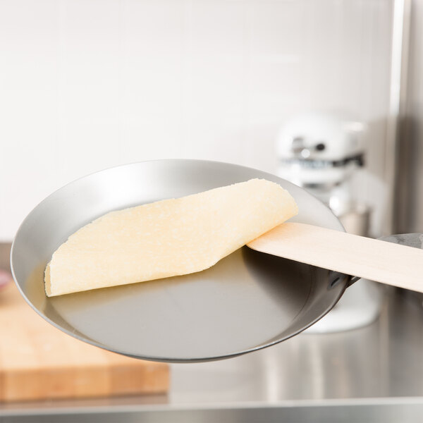 A Matfer Bourgeat black carbon steel crepe pan with a piece of cheese on it.