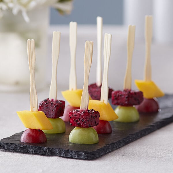 Choice Compostable bamboo fruit picks on a black plate with a variety of fruit.