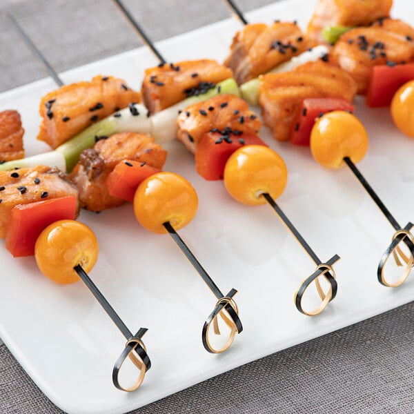 A plate with several black bamboo skewers of food on it.