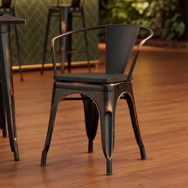 A Lancaster Table & Seating distressed copper metal arm chair with a black wood seat at a table in a coffee shop.