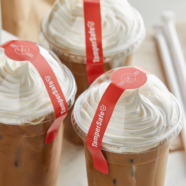 A group of plastic cups with TamperSafe red dome lids and red drink labels filled with coffee and whipped cream.