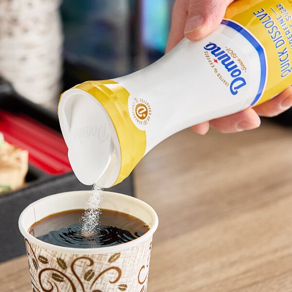 A hand pouring Domino Quick-Dissolve Superfine Sugar into a cup of coffee.
