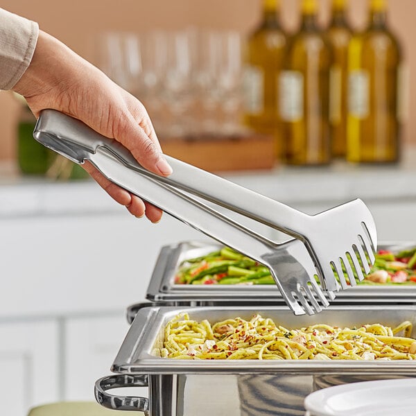 A hand holding Amefa stainless steel serving tongs over food.