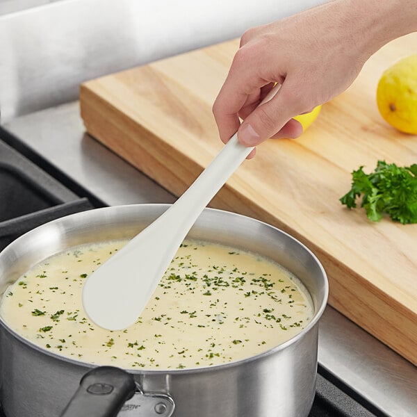 A person stirring soup in a pot with a Mercer Culinary white high temperature spootensil.