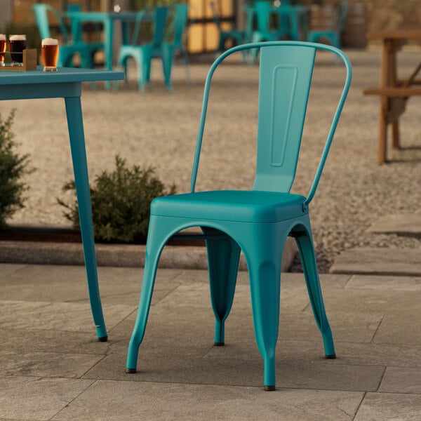 A teal Lancaster Table & Seating outdoor cafe chair on a stone surface.