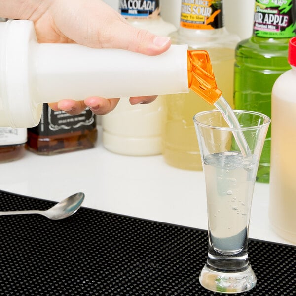 A person pouring liquid from a Carlisle white plastic container with an orange cap into a glass.
