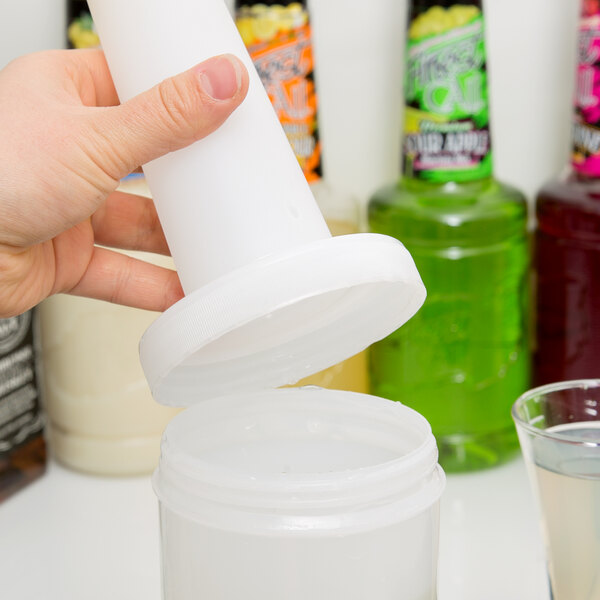 A hand pouring liquid into a white Carlisle plastic container with an orange cap and spout.