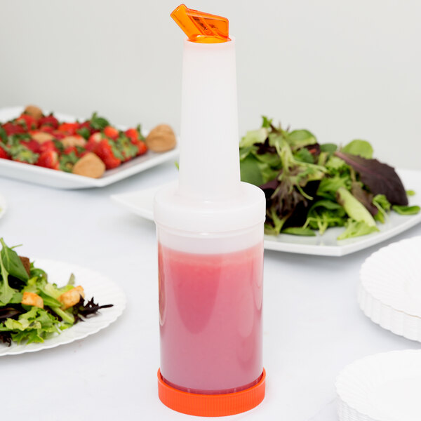 A Carlisle white plastic container with a pink liquid and a white cap on a table with plates of salad.