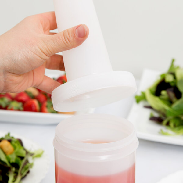 A hand pouring red liquid into a Carlisle white plastic container with an orange lid.