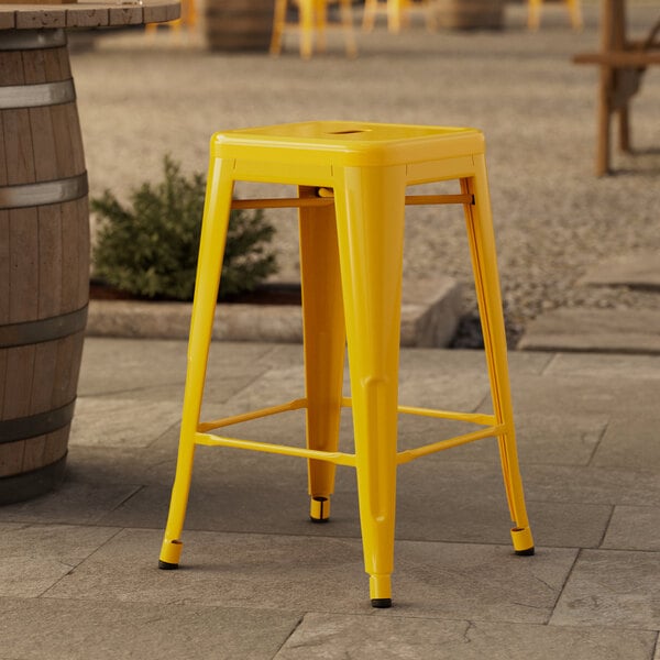 A Lancaster Table & Seating citrine yellow backless counter height stool on a stone patio.