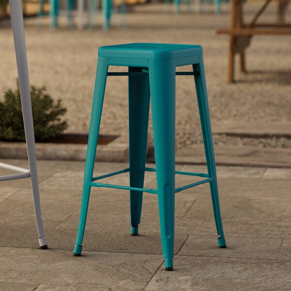 A teal Lancaster Table & Seating bar stool with a seat on a stone surface.