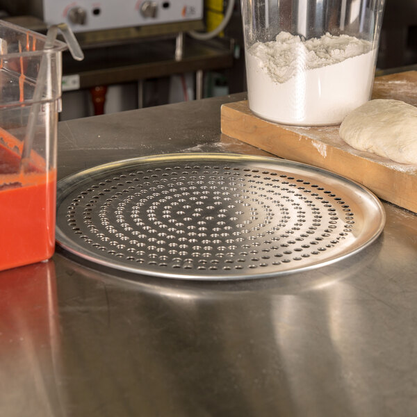 An American Metalcraft Super Perforated Aluminum Pizza Pan with pizza dough on it.